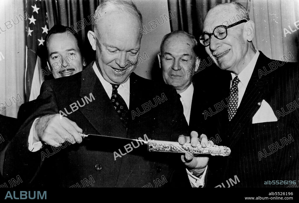 President Eisenhower takes a Uruguayan gaucho knife from its gold and silver sheath after he received the gift today from Joaquin Serratosa Cibils of Montevideo, Uruguay, president of Rotary International. Standing behind them are Spencer Hagen, left, director of public relations for Rotary, and Halsey B. Knapp, Farmingdale, N.Y., first vice president of Rotary. The Rotary president invited Mr. Eisenhower to speak at the golden anniversary convention of the organization in Chicago in May, 1955. February 3, 1954. (Photo by AP Wirephoto).