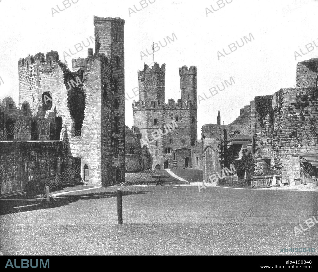 Carnarvon Castle, North Wales, 1894. Carnarvon, or Caernarfon, is a medieval fortress built by King Edward I and dating from 1283. From Beautiful Britain; views of our stately homes. [The Werner Company of Chicago, 1894].