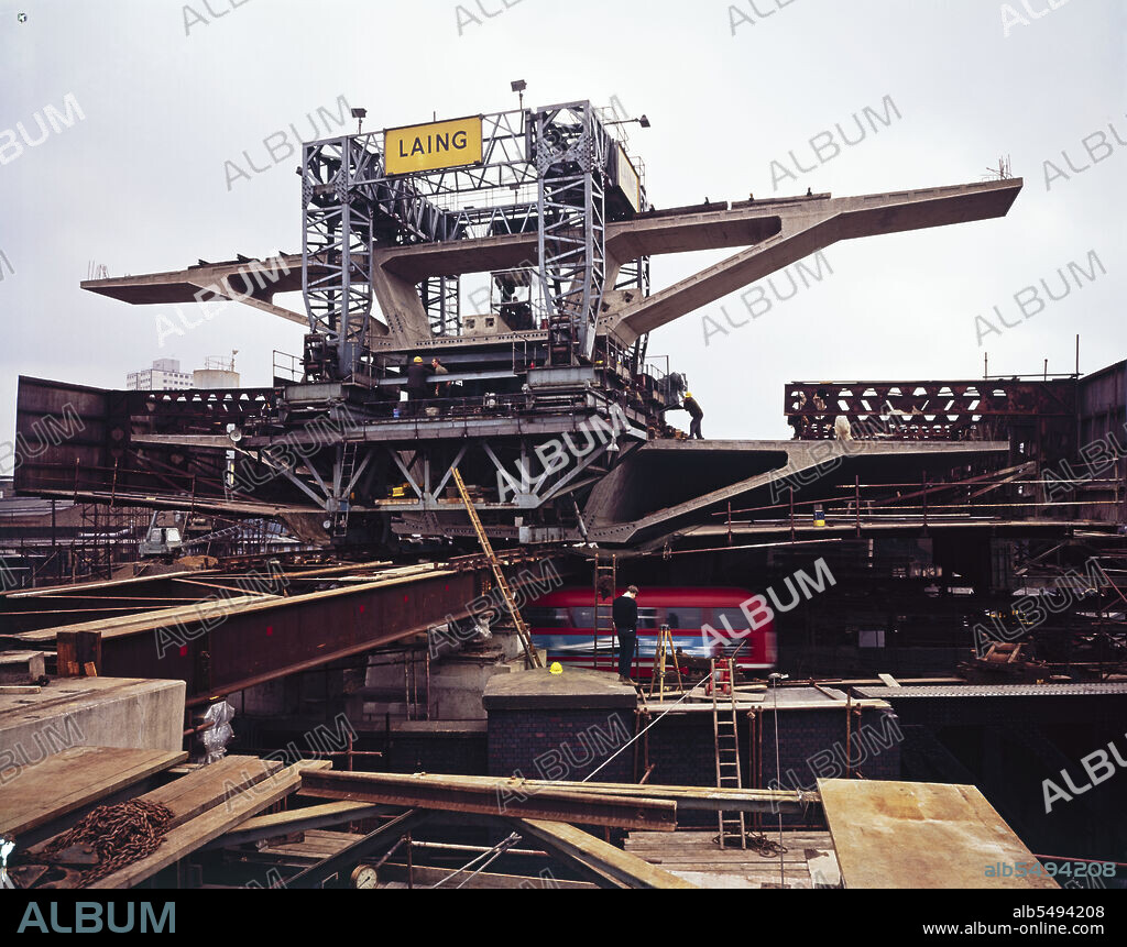 JOHN LAING PLC. Westway Flyover, A40, Paddington, City of Westminster, London, 17/09/1969. The transporter crane lowering a deck unit of the Westway Flyover into place as it spans Great Western Road. The transporter crane was specially designed and built by Laing's Plant Department. The four-legged gantry made 400 trips along the carriageway of Section 5, lifting the individual deck units from the Harrow Road end, transporting them the length of the highway and lowering them into position. The deck units for Section 5 weigh up to 130 tonnes and are more than 28 metres wide, carrying all six lanes of the carriageway. The units are supported on a temporary structure of steel beams weighing 160 tons until each span is complete, stressed together and self-supporting. This photograph was taken at grid reference TQ2491181834.