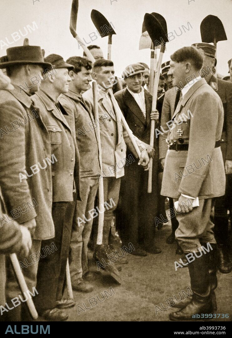 Adolf Hitler chatting to road workers, 1936. Hitler addresses workers in their own factories, and chats with farm hands during harvest time. An informal and frequent scene during road building operations when the Führer chats to road workers. From Germany: The Olympic Year, published. by Volk und Reich Verlag Berlin, 1936.