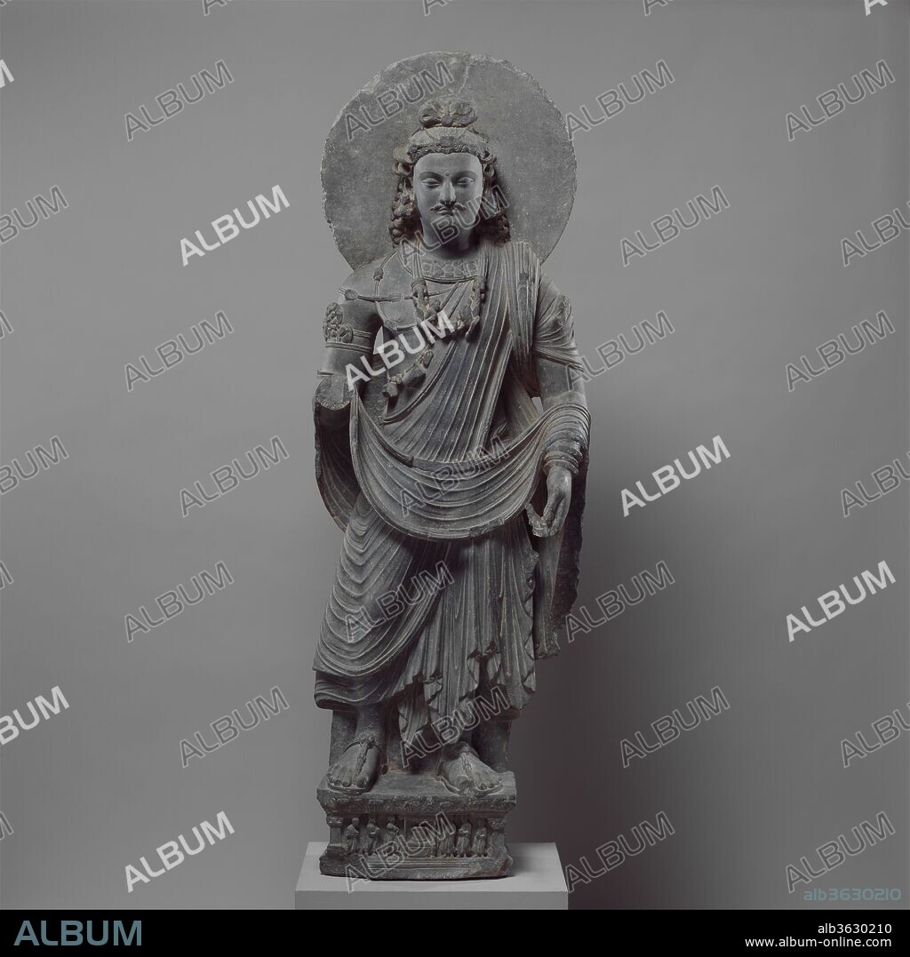 Standing Bodhisattva Maitreya (Buddha of the Future). Culture: Pakistan (ancient region of Gandhara). Dimensions: H. 64 1/4 in. (163.2 cm); W. 21 in. (53.3 cm); D. 8 in. (20.3 cm). Date: ca. 3rd century.
This bodhisattva can be identified as Maitreya by the lip of the sacred water flask in his left hand and by his loop topknot, a hairstyle common to Maitreya images. On the base, donor figures venerate a Buddhist reliquary that rests on a low throne under a canopy.