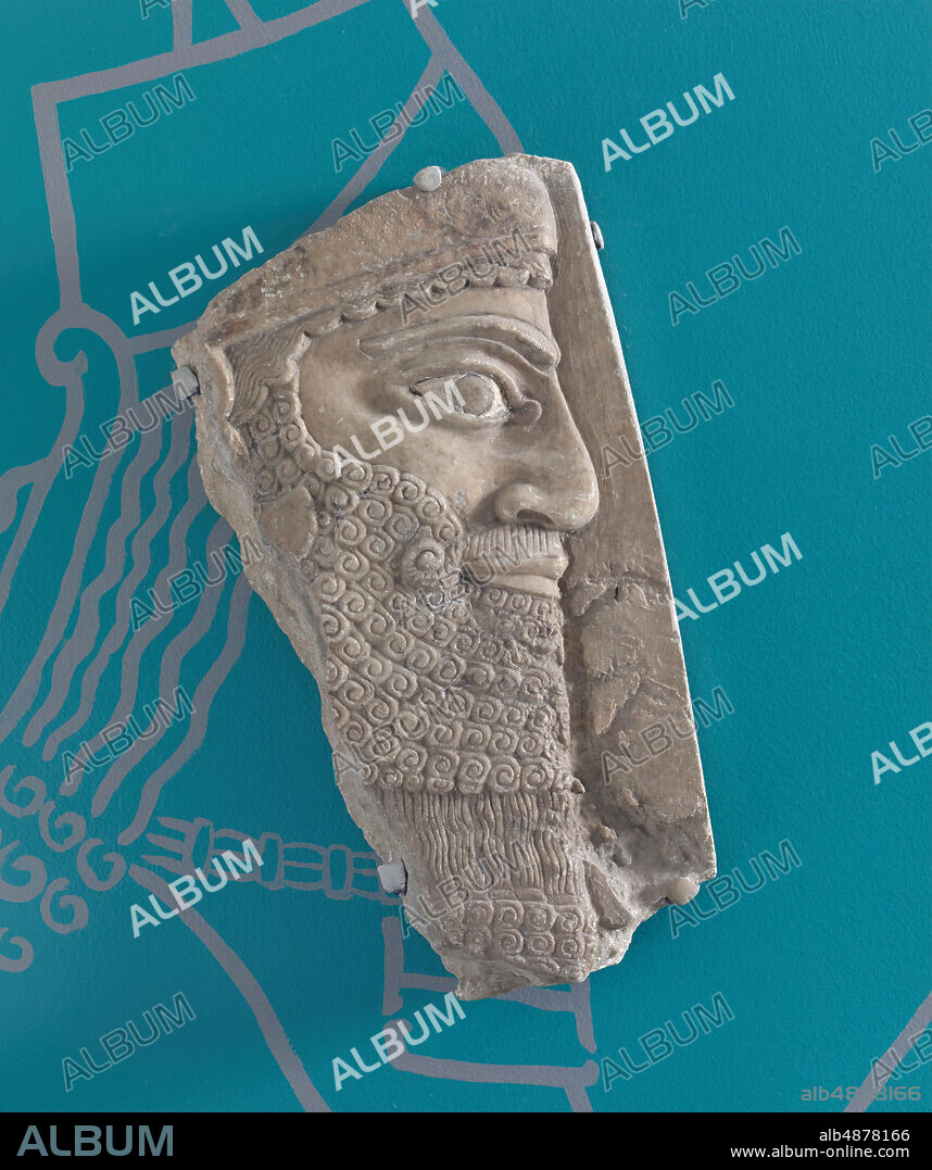 Unknown Artist, Assyrian Relief: Head of Ashurnasirpal II from Kalhu (Nimrud), Iraq, Northwest Palace, Room B, panel 14, ca. 875 - 860 B.C.E., gypsum (Mosul alabaster), 13 9/16 in. x 7 1/16 in. (34.5 cm. x 18 cm.), This portrait of the Assyrian king came from a large relief, the majority of which still resides in Iraq. This portrait once adorned the throne room of the palace. The remarkable state of preservation suggests that the sculpture lay unexposed from the sac of the site, in ca. 614 B.C.E., until its excavation in the nineteenth century. Paint is still visible around the eye, the beard, and decorating the tiara portion of the crown. The large profile eye, prominent nose, and stylized rendition of the beard are all features of the imperial style preferred by the Assyrians. A similar visage was applied to divine figures, thus blurring the lines between regal and divine.