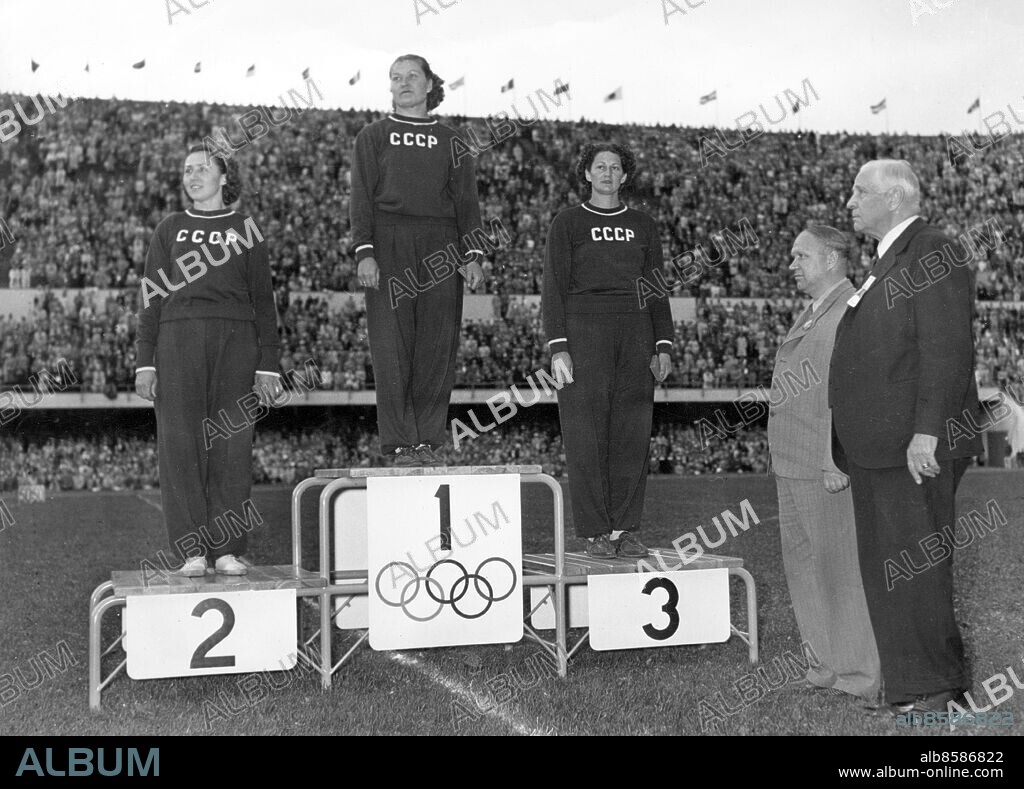 FINLAND HELSINGFORS 1952-07.. Tre sovjetiska medaljörer på prispallen efter damernas diskuskastning vid de olympiska sommarspelen 1952. Här ses från vänster Jelizaveta Bagrjantseva, som kom tvåa, Nina Romasjkova, som vann tävlingen, och Nina Dumbadze, som kom på tredje plats.Th ses Sigfrid Edström, svensk f.d. ordförande i IOK.. Foto: Olympia-Kuva / AB Text & Bilder / SVT / Kod: 5600. Finsk och engelsk originalbildtext.. Mapp: Diskus (O.S. 1952) I:286q. Trio Vinnare Segrare Prisutdelningar Prispallar.