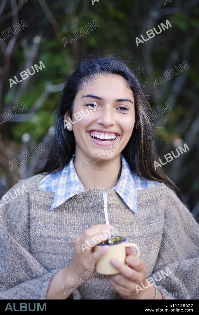 A Patagonian girl in a traditional wool poncho with a bombilla straw drinking yerba mate, Patagonia, Chile, South America.