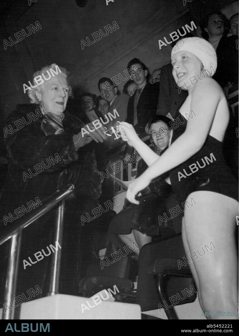 Celia Sandys, 9, receives a cup from her grandmother, Lady Churchill, after winning a one length free-style race for under-ten's at the international gala.At the Marshall-street Baths, Westminster, last night Celia Sandys, 9, daughter of the Minister of Supply, Mr. Duncan Sandys, won one of the Mermaid Club races - and received a little silver cup from her grandmother, Lady Churchill. February 1, 1954. (Photo by Daily Mirror).