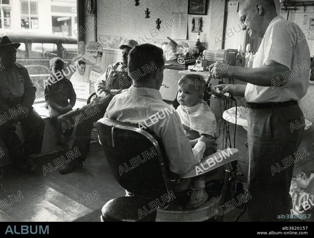 Arch Pugh barber shop in Palmyra, Missouri, where a two-year-old boy, held by his father, gets a haircut. This picture was taken in 1952.