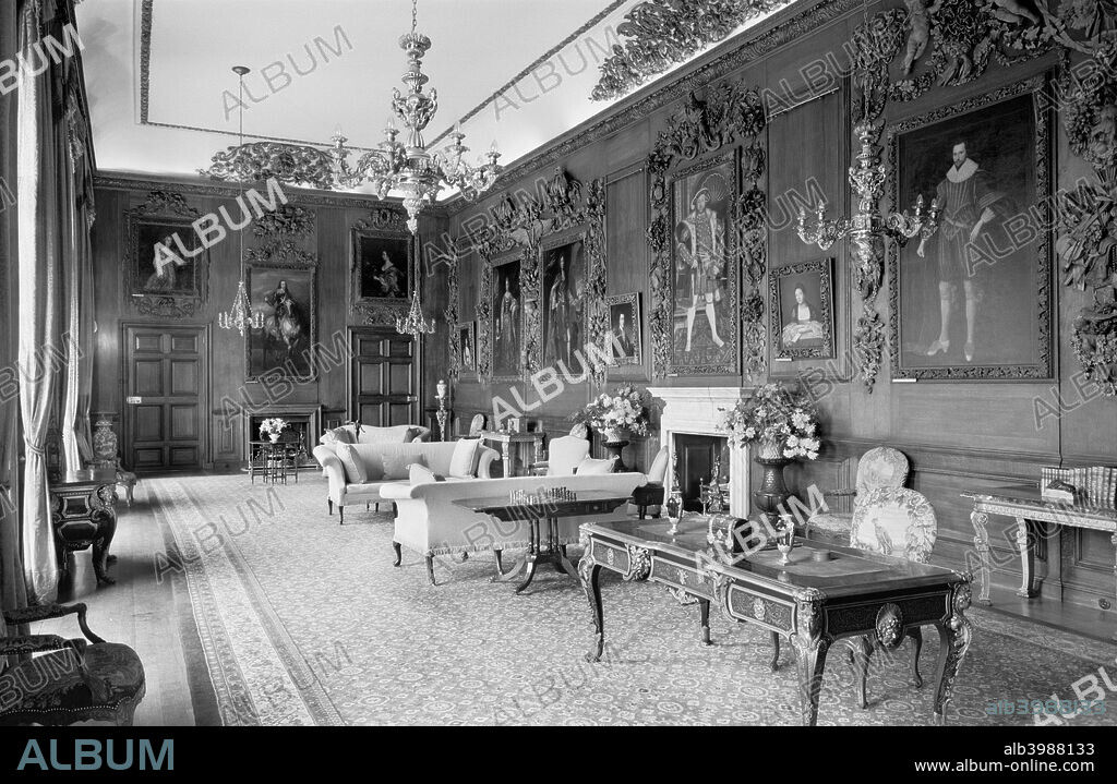 Petworth House, Petworth, West Sussex, 1945-1980. Interior of the Carved Room at Petworth House. Petworth was extensively remodelled in the late 17th century, but this room was probably redesigned a century later. The portraits which line the walls are surrounded by elaborate carving by Grinling Gibbons and others.