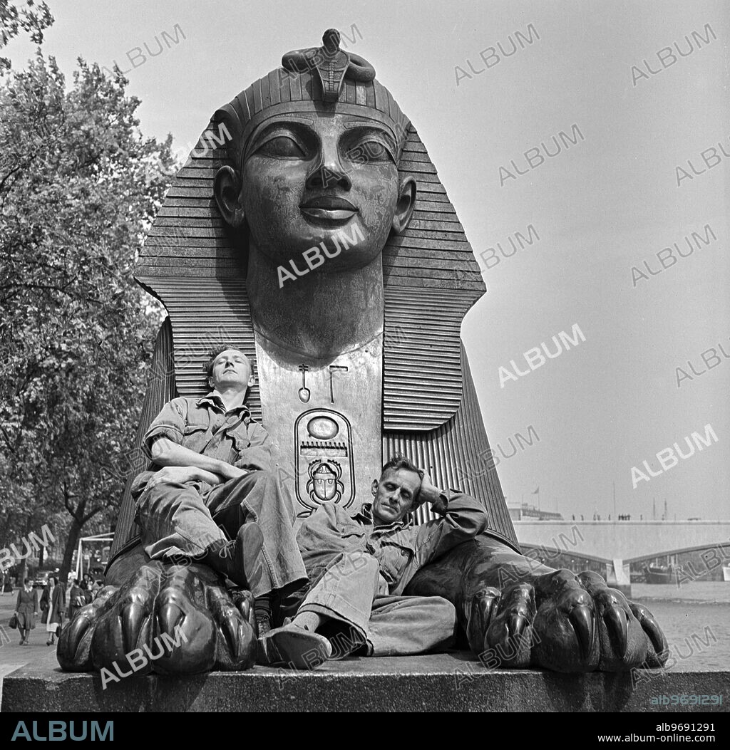 London Siesta. Two workmen , finding the Embankment seats occupied , have fallen asleep in the lap of London's Sphinx , guarding Cleopatra's Needle , obelisk near Waterloo Bridge . 1950.