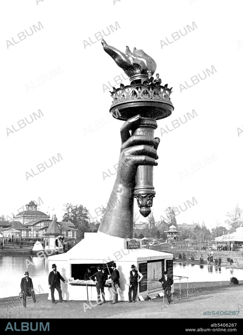 The torch and part of the arm of the Statue of Liberty, on display at the 1876 Centennial Exhibition in Philadelphia. Information booth at base of arm and two persons seen at railing below flame of torch. The Statue of Liberty is a colossal neoclassical sculpture on Liberty Island in New York Harbor, designed by Frédéric Bartholdi and dedicated on October 28, 1886. The statue, a gift to the United States from the people of France, is of a robed female figure representing Libertas, the Roman goddess of freedom, who bears a torch and a tabula ansata upon which is inscribed the date of the American Declaration of Independence, July 4, 1776. The statue is an icon of freedom and of the United States: a welcoming signal to immigrants arriving from abroad. Cropped stereograph Centennial Photographic Co., 1876 (cleaned).