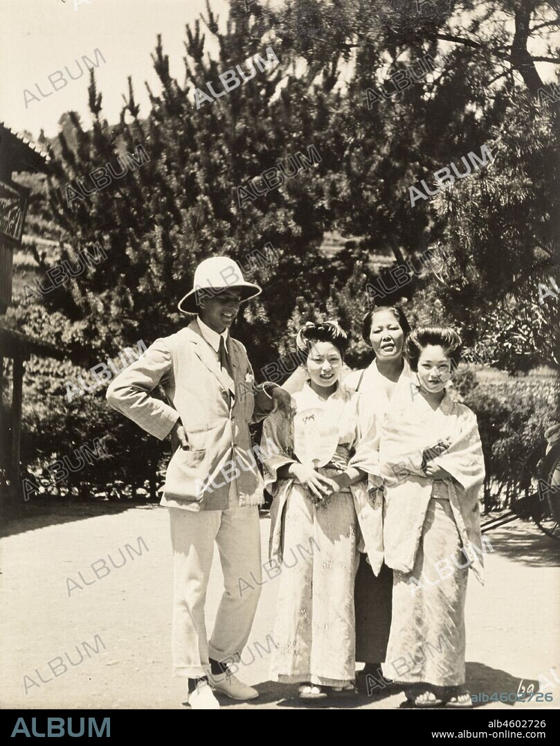 Japan, A European man poses outside a Japanese tea house with two female geisha and their 'okaa-san' (the female manager of a geisha house). The girls wear traditional kimonos and their hair is worn up in 'shimada' style. Original manuscript caption: Moji - Tea House girls and Mamma, & "our allies", circa 1920. 1998/028/1/1/270.
