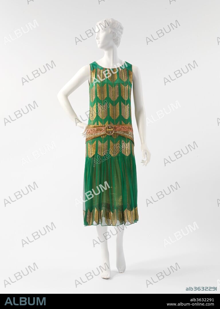 "Arrow of Gold". Culture: French. Designer: Paul Poiret (French, Paris 1879-1944 Paris). Date: 1925.
The influence of the 1925 Exposition Internationale des Arts Décoratifs et Industriels Modernes on fashion was especially pronounced in textile designs of the period. The green silk chiffon of the gown is brocaded with a gilt-thread fletching motif in overall repeat on the torso of the dress and on the hem. Renowned as a colorist, Poiret is unusual among couturiers in his advocacy of vivid green as a fashionable hue. In various tonalities, green is represented in almost all of the designer's collections. Here, Poiret has complemented the color with a hip girdle of pink and gold that brings to the surface of the dress the colors of its richly brocaded pink silk underdress in the kind of sophisticated juxtaposition for which the designer was celebrated. 
Poiret has created a tunic proportion, favored in the period, by extending the bodice to the lower hipline, where the skirt is then shirred in a dagged line conforming to the fletching motif. The sashlike girdle is positioned along the upper hipline, which not only introduces a more personalized proportion but also mediates Poiret's concession to prevailing modes. An almost intransigent, deliberately individualistic approach to design therefore appears in even his most conventional works. Poiret's lifelong assertion of his identity as an artist subordinated his pursuit of commercial success. Thus, although arguably with increasing subtlety, idiosyncracy infused his designs until the close of his couture house in 1929.