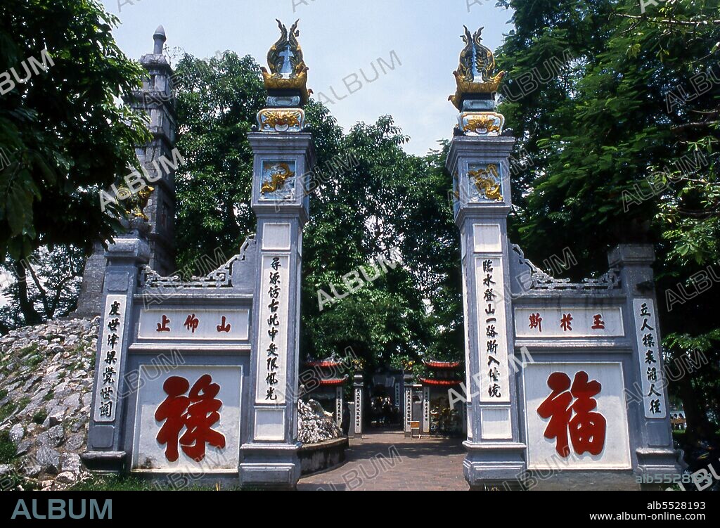 Den Ngoc Son, or ‘Jade Mountain Temple’ is one of the most revered religious complexes in the capital. Established by the scholarly mandarin Nguyen Van Sieu (1799–1872) appropriate symbols of learning and literature mark the temple complex. A stylised stone ink slab rests atop the arched gate at the entrance; nearby a tapering stone pillar representing a traditional Chinese brush pen rises through five levels. On its side, three Chinese ideograms proclaim <i>ta thanh thien</i>, or ‘writing on a clear sky’. Beyond the entrance, a red-painted, gracefully arched wooden bridge leads across the still green waters to a small island in the north of the lake. This is the celebrated <i>The Huc</i> or ‘Rising Sun’ Bridge, where groups of Vietnamese children often huddle hoping to catch a glimpse of one of the lake’s legendary turtles.