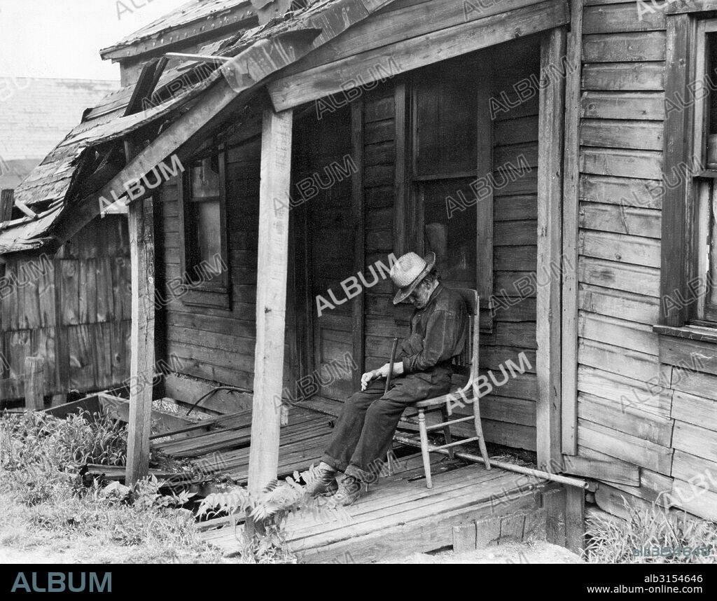 Washington, Pennsylvania:  1936. A very old man doses in a chair on the front  porch of a dilapidated shack of a home.