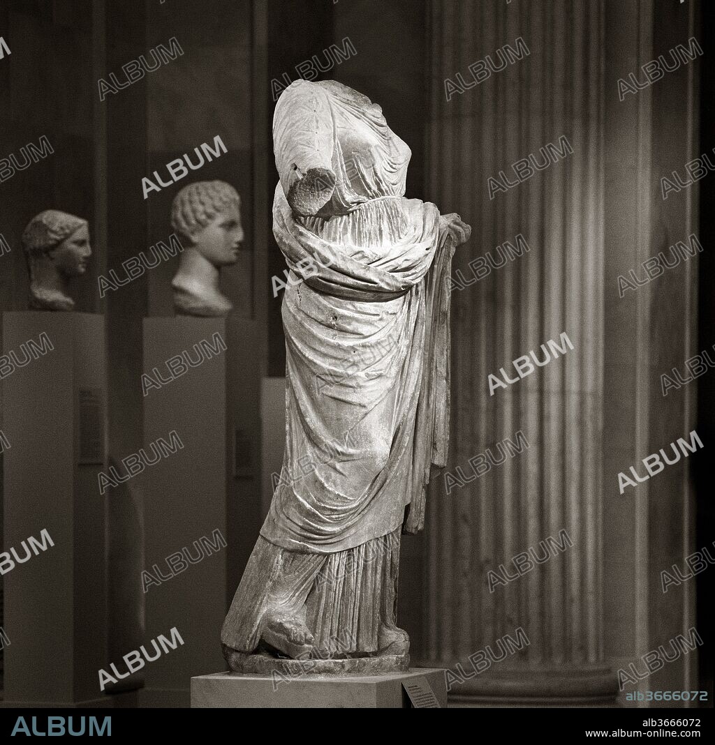 Marble statue of a woman. Culture: Greek. Dimensions: Overall (H. w/ plinth): 68 1/8 in. (173 cm)
H. (H. without plinth): 66 1/8 in. (168 cm). Date: 2nd half of the 4th century B.C..
The lively, varied manner in which the texture of the clothing is rendered suggests that this is a Greek original rather than a Roman copy. The crinkly linen of the chiton and the heavier wool of the himation (cloak) are carefully differentiated, and horizontal press folds add variety to the latter's surface. The drilled holes on the sleeves once held metal buttons. The upper part of the chiton is kept firmly in place by a cord that is crossed in back and slipped over the arms. This over-life size figure probably represents a goddess, and in the absence of other attributes, the shoulder cord may offer a clue to her identity. Although the huntress Artemis is often shown with such a cord, this more matronly figure may represent Themis, a goddess associated with custom and law. The head and neck were carved separately and provided with a rounded tenon that was set into the cavity at the top of the torso.