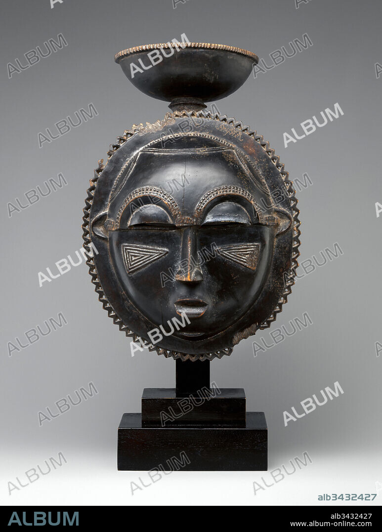 Moon Mask, ca. 1880, Côte d'Ivoire, Baule peoples, Wood, H. 10 1/2 × W. 6 3/4 × D. 5 1/4 in. (26.7 × 17.1 × 13.3 cm), Wood-Sculpture, This Baule mask features a perfectly round, domed face framed by a flat rim bordered with a pierced serrated decoration, echoing the zigzag border of a cup delicately balanced at the summit. The crescent eyes, slender nose, naturalistic mouth, and a panel of concentric triangles carved in relief on each cheek contribute to the refined composition.