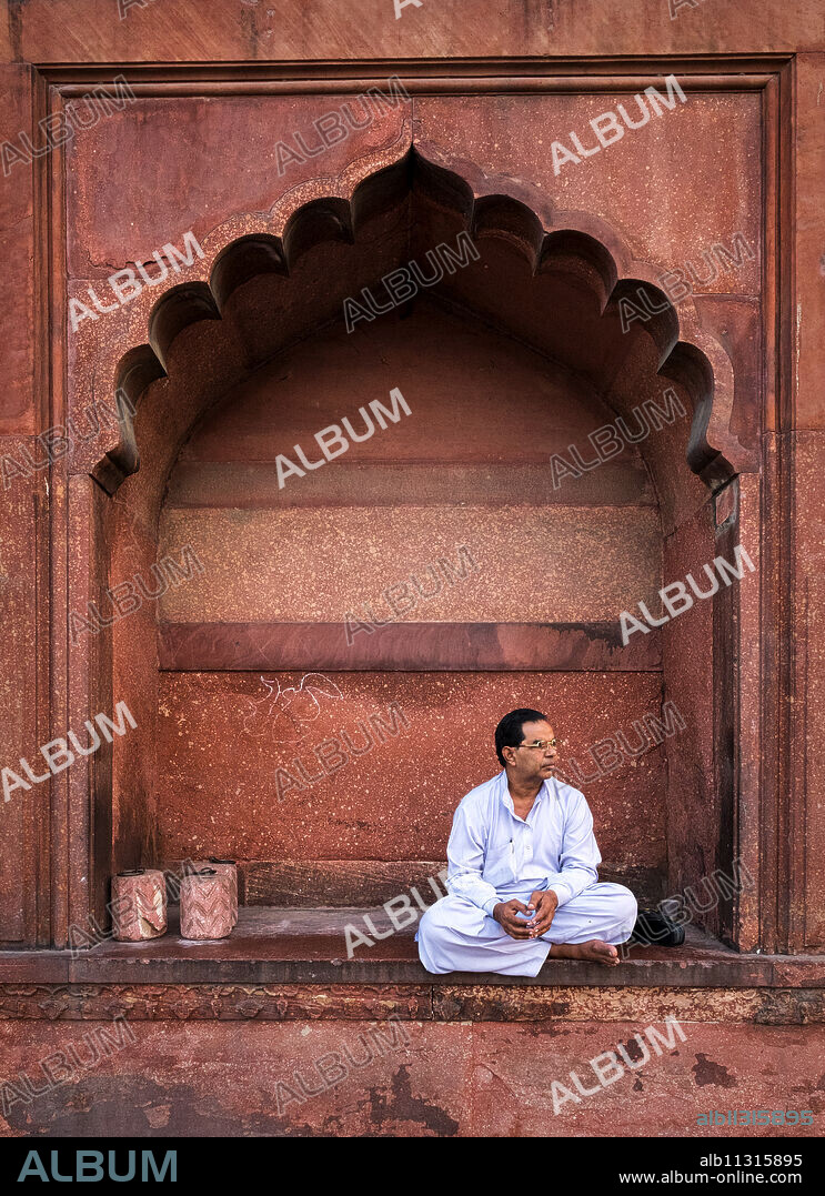 Man sitting in arch at Jama Masjid mosque in Delhi, India, Asia.