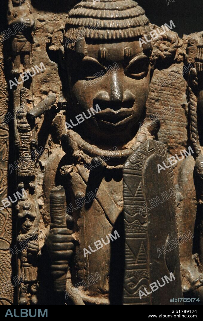 ARTE AFRICANO. NIGERIA. S. XVI. BRONCES DE BENIN. Detalle de un bronce que muestra la FACHADA DEL PALACIO REAL DE BENIN CON ESCENA DE CORTE Y PROTOCOLO. Detalle de un GUARDIAN. Estarían ubicados en los pilares que sostendrían la cubierta del Palacio Real de Benin. Bronce o latón. Museo Británico. Londres. Inglaterra. Reino Unido.