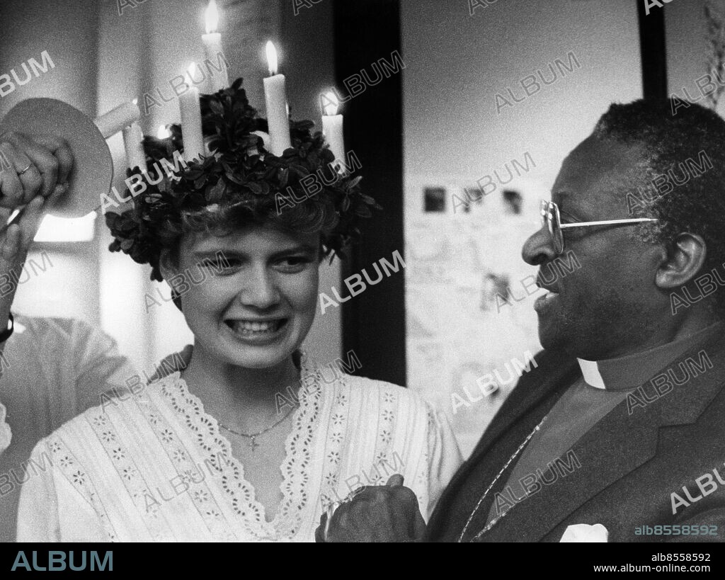 UPPSALA 19841213 . Biskop Desmond Tutu, Sydafrika, vinnare av Nobels fredspris 1984, iakttar när lucian Annette Linde får sina ljus tända i Kyrkans hus i Uppsala. Hastande mellan presskonferens och föreläsningar blev detta ett improviserat lussande för Tutu.. Foto: Olle Seijbold / DN / TT / Kod: 51. **SVD OUT**.
