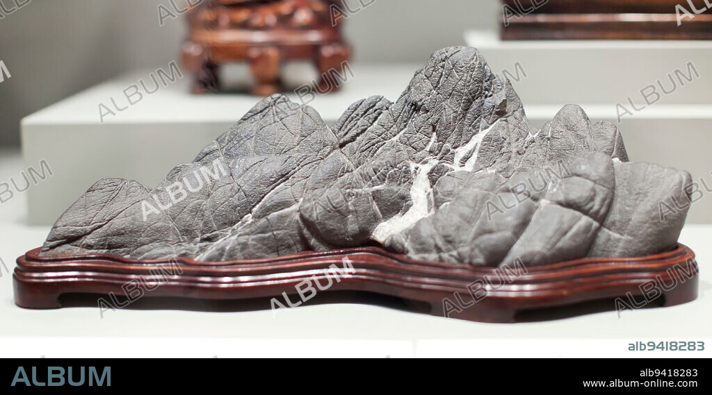 Scholar's Rock, 19th century, 6 9/16 x 17 1/2 x 8 7/16 in. (16.67 x 44.45 x 21.43 cm) (including stand), Ying stone, China, 19th century, This intricately wrinkled and textured ying stone is a classic example of a 'distant view mountain' rock. Deep crevices traverse the rock's middle giving it the impression of several mountain peaks separated by gorges. The white calcite inclusion approximates the look of a mountain glacier. Miniature mountain landscapes form a sub-category of scholar's rocks. More reflective of the natural environment than the dramatically convoluted and perforated ling-pi and tai-hu scholar's rocks, they were perfect for studios that lacked views of a distant landscape.