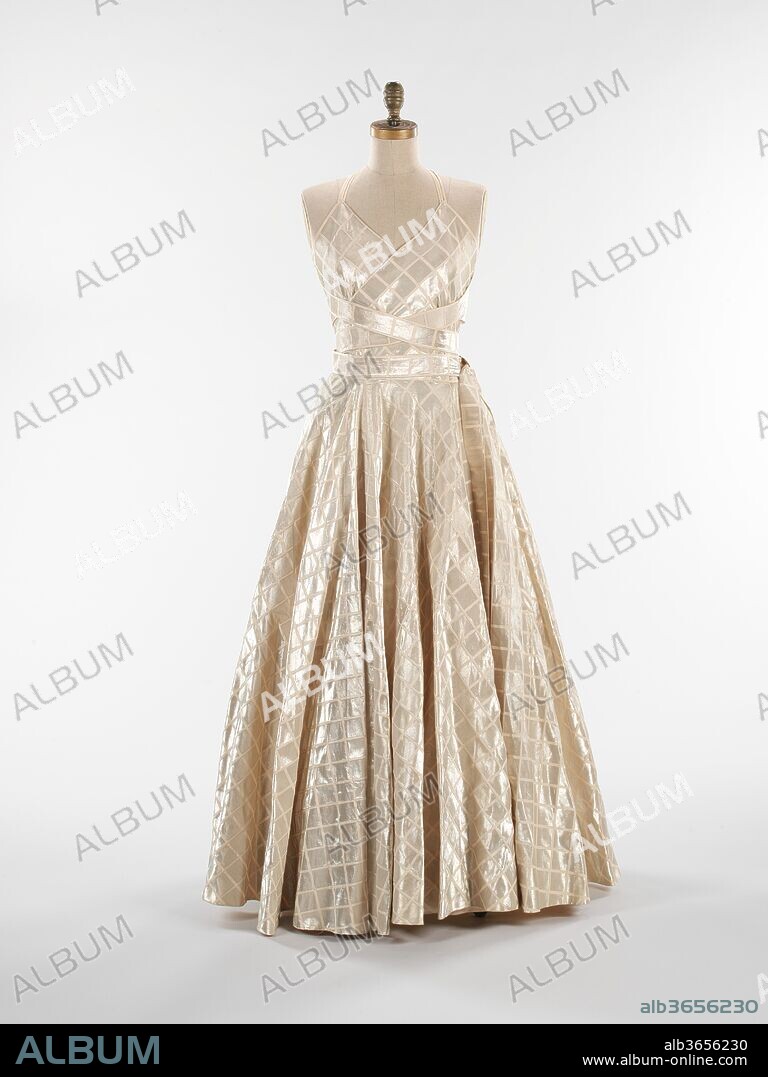 Evening dress. Culture: French. Design House: House of Lanvin (French, founded 1889). Designer: Jeanne Lanvin (French, 1867-1946). Date: fall/winter 1938-39.
This shimmering dress presents a well-planned design which highly emphasizes the sheer crisp quality of its textile.  The brilliant back drapery creates the feel of a vest evoking clothing of the Middle East while the front presents a strictly high fashion silhouette of the period.  
Jeanne Lanvin was apprenticed to a milliner and a dressmaker before opening her own millinery shop in 1889.  She expanded into dressmaking when her clients began asking for the ensembles in which she adorned her daughter, Marguerite di Pietro (1897-1958).  Her style embodied the femininity of youth in a most modern way with meticulous and relatively sparse surface embellishments and robe de style silhouettes, which could be worn by women of all ages.  Lanvin's aptitude can be seen through her house's 1920s expansion into fur, lingerie, men's wear, household goods and perfume. She even had the forethought to open her own dye factory which produced the inimitable 'Lanvin blue.'  The longevity of the House of Lanvin can be credited to her attentive management and design standards from its inception.