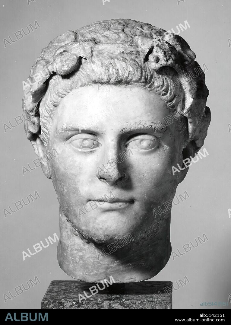 Portrait of an Roman, Formerly Johannes W. F. Collection Reimers (Hamburg), Marble, chiseled, drilled, smoothed, marble, Total: Height: 30 cm; Width: 24.5 cm; Depth: 25 cm, Sculptures, Three-dimensional sculptures, Man, Head, Face, Head image, Hair curl, tuft, strand, Hair fashion, Hair fashion, Wreath, Garland, Portrait, Priest, Soldier Emperor, Roman Antiquity, The portrait formerly belonged to a bust or statue. The antique break at the neck has been worked off in a modern way as a surface to allow a better base. The face must have been cleaned with acid in more recent times, while the hair and the wreath were left in the state in which they were found. The reddish-brown earth deposits are clearly visible. The contrast between the specky-glossy face and the dull hair and wreath leaves results from this different treatment. Depicted is a man of younger age with a throat beard, a beard costume, which is particularly well known from portraits of the Roman emperor Gallienus (reigned 253-268 AD). The portrait of the man shown here also belongs to these years. The ivy wreath in his hair seems to indicate a connection with the wine god Dionysos (lat. Bacchus), whose attributes include ivy or vine wreaths. The high sculptural quality of the head is particularly expressed in the naturalistic formation of the wreath leaves. The elaboration of the portrait becomes more summary towards the back. From this it may be concluded that the portrait was originally placed in front of a wall or in a niche, so that the rear view was hidden from the viewer.