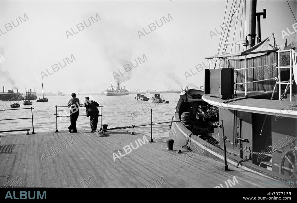 Shipping on the River Thames at Gravesend Reach, Kent, c1945-c1965.  Looking up river from the Royal Terrace Pier, with a boat moored alongside the pier and two men leaning on the rail watching the scene.