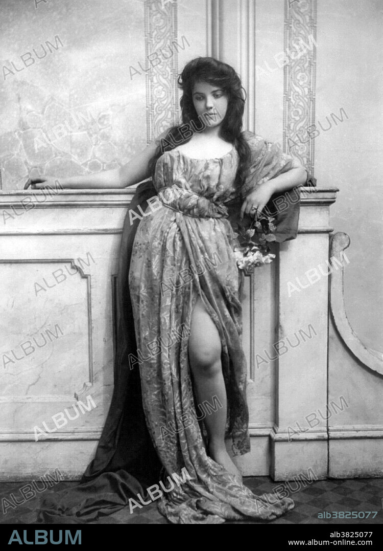 Entitled: "Young woman modeling, leaning on mantle and wearing split skirt." Fashion is a popular style or practice, especially in clothing, footwear, accessories, makeup, or furniture. Fashion is a distinctive and often habitual trend in the style in which a person dresses. It is the prevailing styles in behavior and the newest creations of textile designers. Prior to the mid-19th century, most clothing was custom-made. It was handmade for individuals, either as home production or on order from dressmakers and tailors. By the beginning of the 20th century, with the rise of new technologies such as the sewing machine, the development of the factory system of production, and the emergence of department stores, clothing had increasingly come to be mass-produced in standard sizes and sold at fixed prices. Photographed by Fitz W. Guerin, 1902.