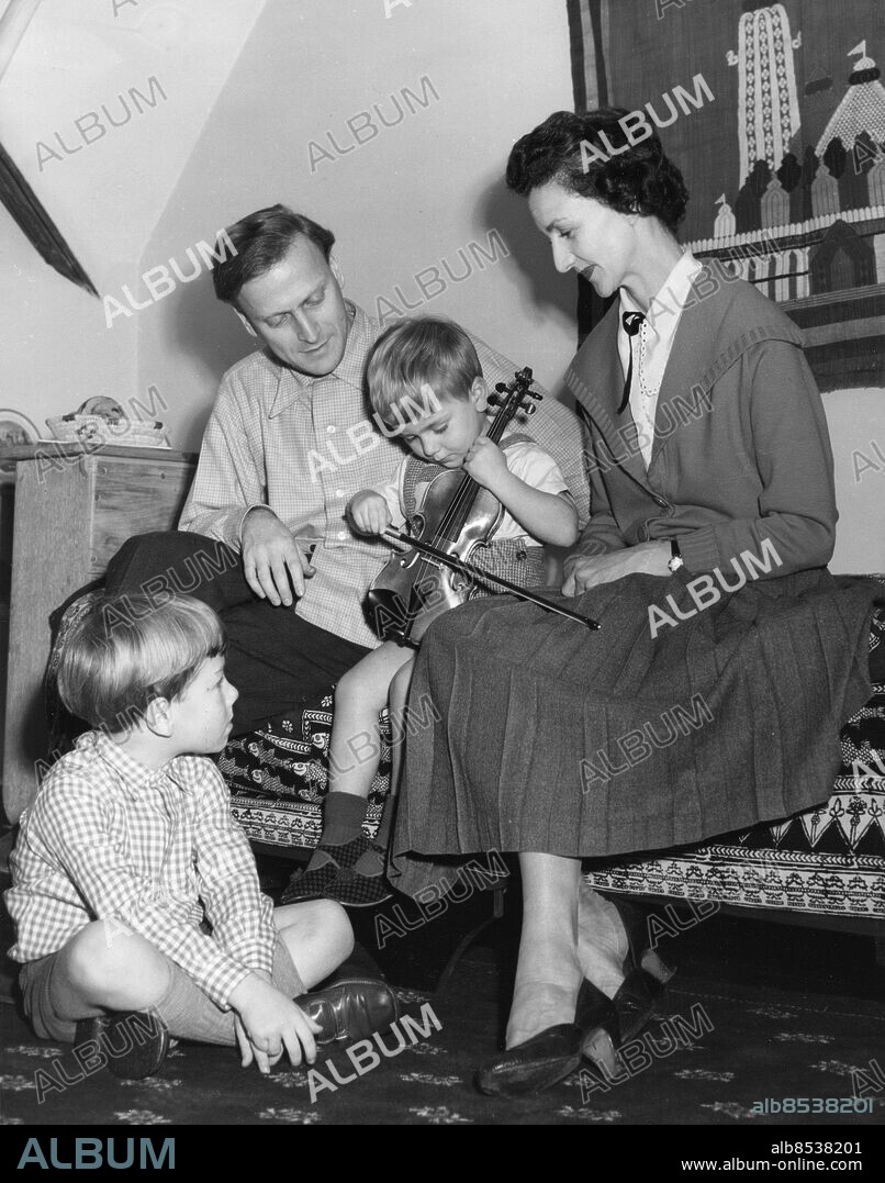 Orig. bildtext... ANOTHER GENIUS IN THE FAMILY? The celebrated violinist, Yehudi Menuhin is now in London for recitals of Beethoven's sonatas. In fact he's been in London some time, but the public meet him only at the concerts. He does not seek publicity in other ways. Thirty eight year-old Menuhin was born in New York. His parents are of Russian origin who went to America from Palestine. He was given his first violin at the age of four. When he was seven he startled an audience who heard him play a Mendelssohn concerto with the San Francisco Symphony Orchestra, at ten he played at Carnegie Hall. His first appearance in England was at the famous Queen's Hall in 1929. His home is the family ranch in California but with him in London are his wife and two boys, Gerald, aged six, and Jeremy, three. Asked recently what it was like to be the wife of a genius, Mrs. Menuhin, (the English-born former ballerina, Diana Gould) said If its salvery to be a genius, its worse salvery to be his wife! I am wife-mother, companion, travel agent, packer, valet, and secretary... See companion picture. Photo shows. The Menuhin family at their London home. Yehudi watches his youngest son try out a small violin. Maybe there will be three genius's in the family soon. Dec. 13.54. Anm. Y Menuhin, 1916-1999, amerikansk-brittisk violinist, musikaliskt underbarn. D Gould, 1912-2003, brittisk dansös, Menuhins andra hustru. Fioler Helveckat Kortbyxor Musicera Stolta föräldrar CD669 persons: JEREMY MENUHIN;DIANA GOULD;GERALD MENUHIN;YEHUDI MENUHIN sites: LONDON;USA*;STORBRITANNIEN.