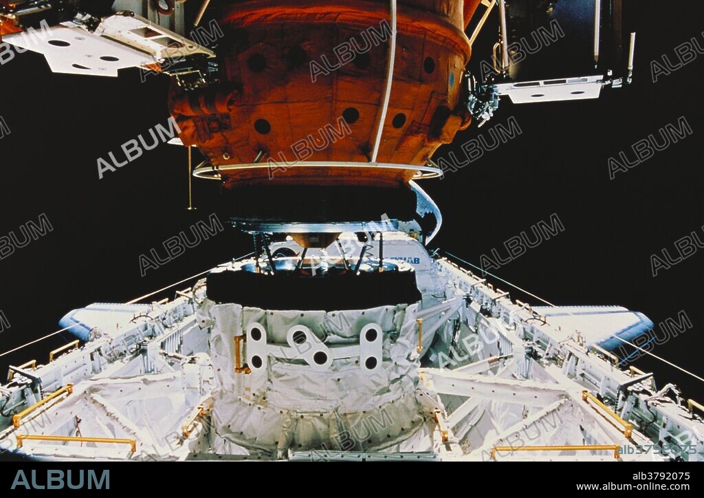 The docking module, (orange), and the Orbiter docking system, (at lower center), during the docking of the Space Station Mir with the Space Shuttle Atlantis, (in the lower frame). The docking module is attached to Mir, while the Orbiter docking system is part of Atlantis. Photographed on March 24th, 1996, during Mission STS-76.