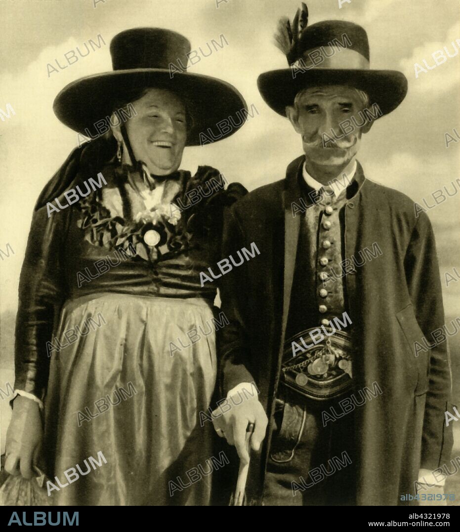 Couple in traditional dress, Sankt Lambrecht, Styria, Austria, c1935. Woman in wide-brimmed hat, and man wearing lederhosen, from the village of Sankt Lambrecht. From "Österreich - Land Und Volk", (Austria, Land and People). [R. Lechner (Wilhelm Müller), Vienna, c1935].
