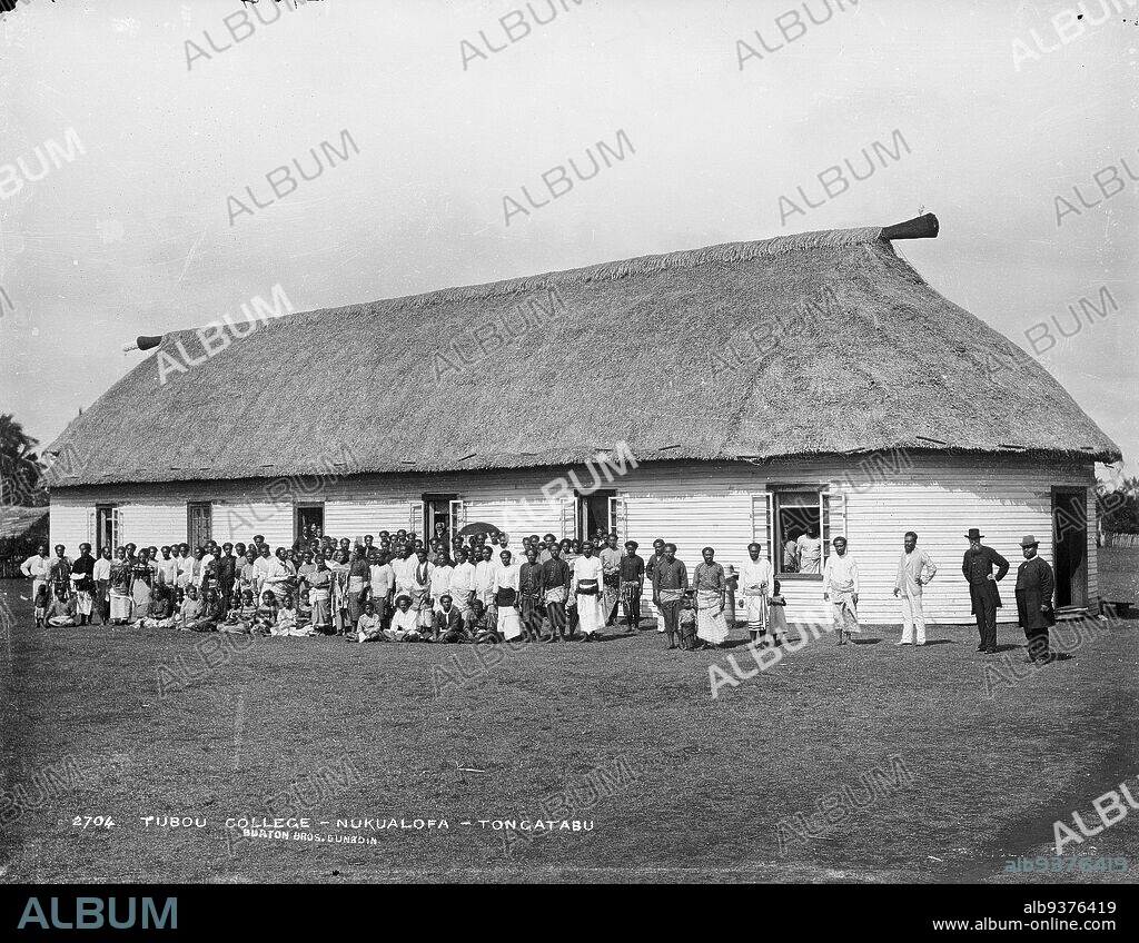 Tubou College, Nukualofa, Tongatabu [Nuku'alofa, Tongatapu], Burton Brothers studio, photography studio, 29 July 1884, New Zealand, black-and-white photography, Large building with wooden walls and Fale styled roof, door way at right, and six double windows (open) run down side. In foreground a clearing with a large group of people either sitting or standing in rows in front of building. Some people are visible in the windows.