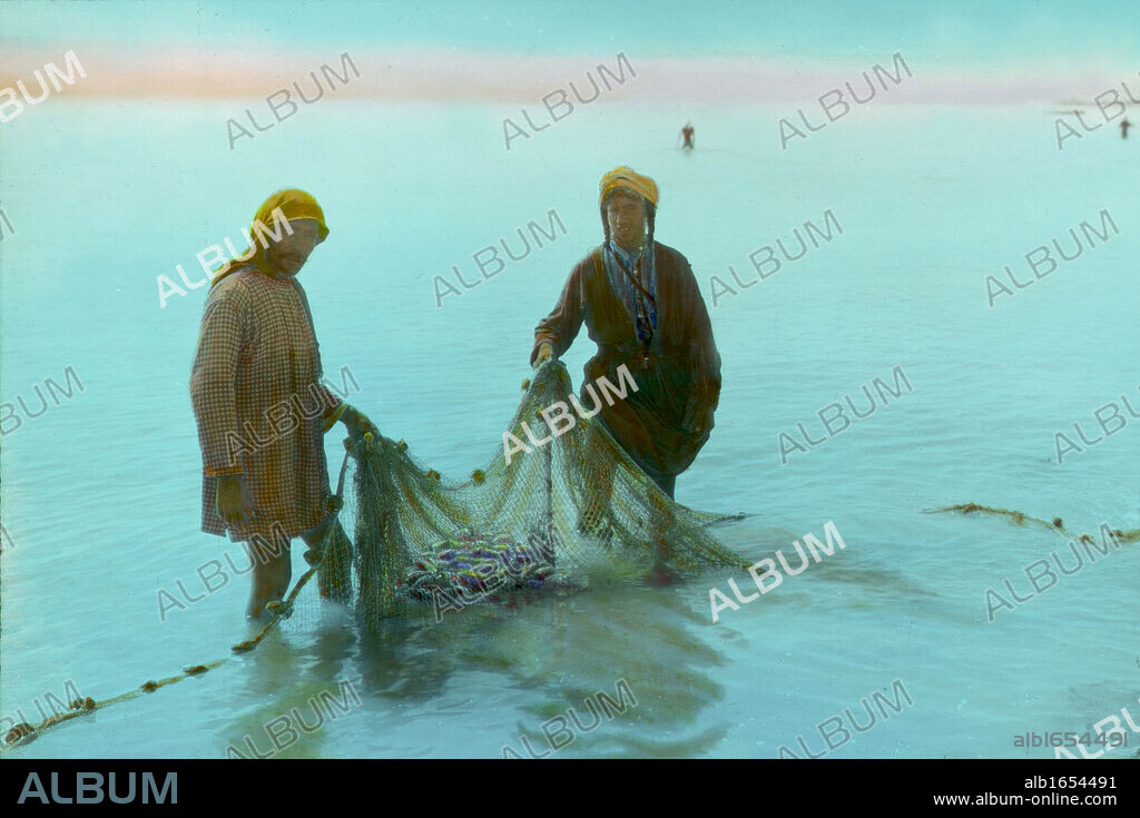 Fishermen hauling in their nets, Sea of Galilee (Lake Gennesaret , Lake Kinneret) the lowest freshwater lake in the world and largest freshwater lake in Israel. Hand-tinted photograph, early to mid 20th century. Palestine Fishing.