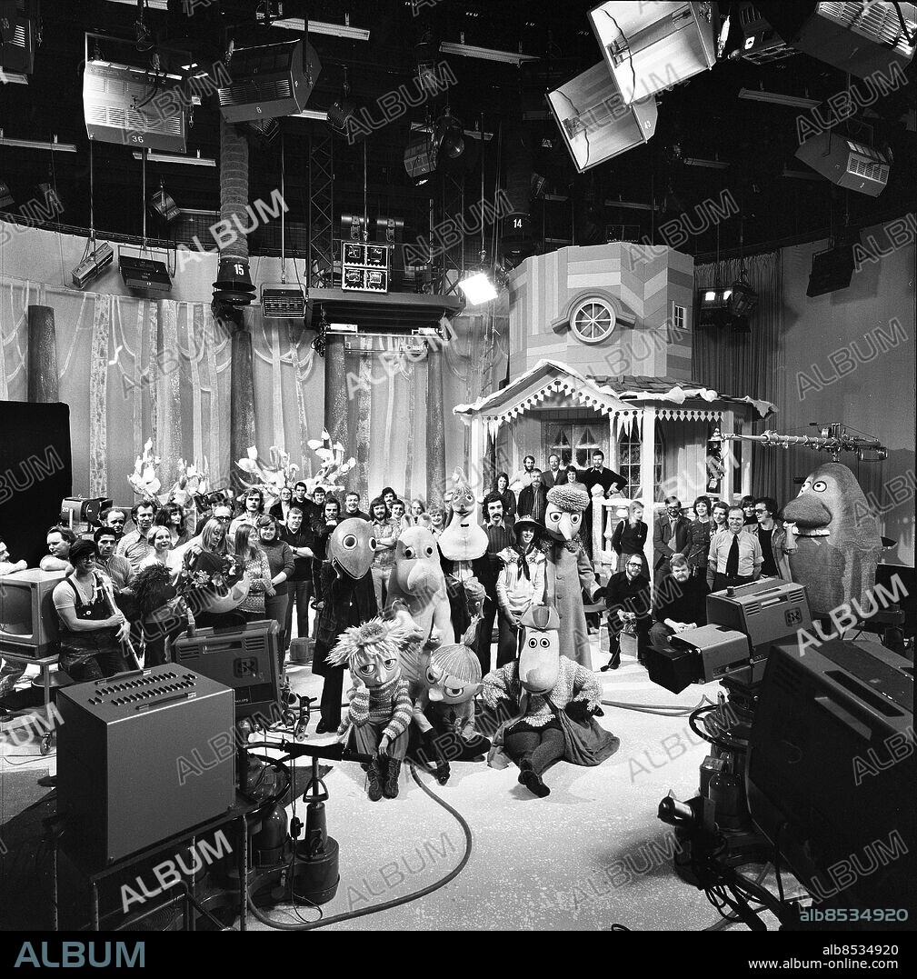 1973-09-25.. Reportage inför JULKALENDERN: MUMINDALEN. TV-program av Tove och Lars Janson i regi av Pi Lind och Ingegerd Lönnroth.. Sänt första gången 1973-12-01.. Här ses i förgrunden några av Mumindalens innevånare. Runt dem grupperar sig från vänster till höger: ateljégruppen med scenogafer, kostymörer, snickare och målare, teknisk personal (kameramän och andra). På och framför verandan syns rekvisitörer och ljussättare, till höger om dem vid verandaräcket produktionsgruppen med regissören Pi Lind i mitten och framför dem ljudgruppen och till slut Mårran.. Foto: Bertil S-son Åberg / RiR / SVT / Kod: 5600. Bild och reportage publ. i RiR 49/73 sid. 6-9.. RiR 20973 sv/v neg   . Adventskalender.