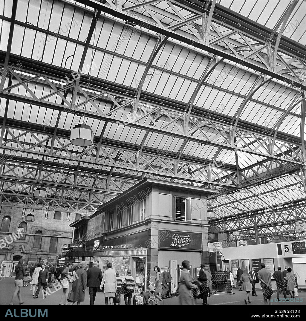Charing Cross Station, London, 1960-1972. Passengers on the station concourse outside platform 5, with a branch of Boots the chemist.
