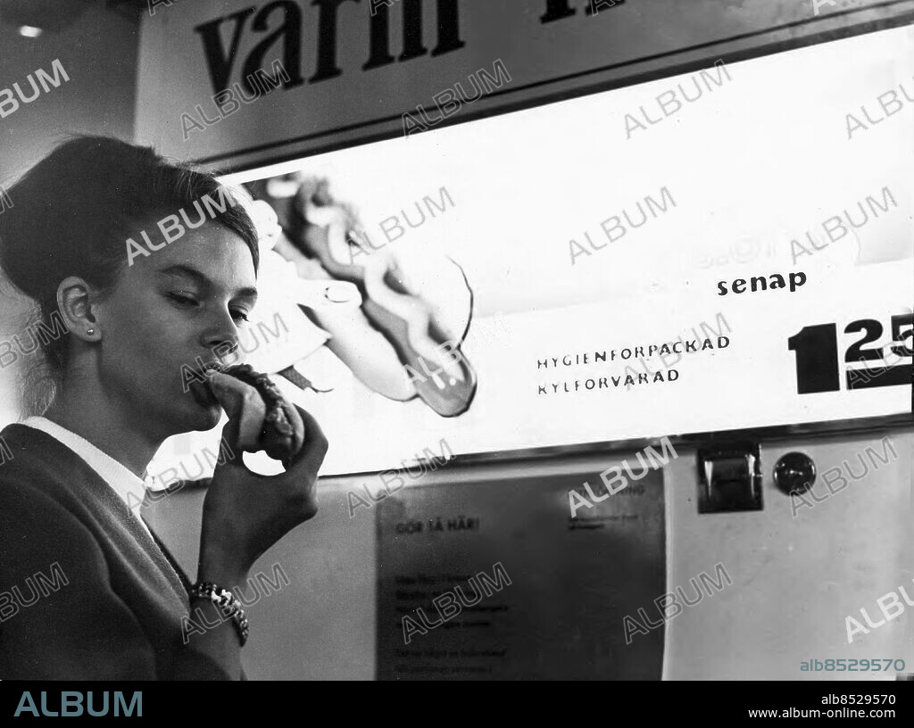 Stockholm 1964-07-30. Automat med varmkorv. Den som stoppar 1 krona och 25 öre i myntinkastet har på några sekunder en varm korv i nypan. På bilden ses Margareta Larnholt smaka en elektronkokad korv på en tunnelbanestation i Stockholm.. Foto: Expressen / TT / Kod: 192. ** AFTONBLADET OUT **.