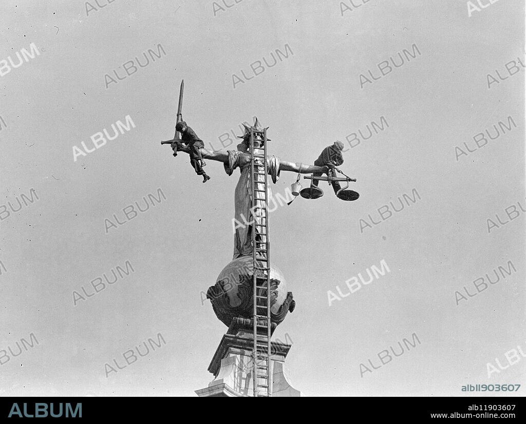 Balanced in the scales of "justice". Clambering over the outstretched arms of justice and standing nonchalantly in her very scales, workmen are re-gilding for the Coronation the famous statue which surmounts the Old Bailey. Photo shows: a workman standing in scales and another holding onto the sword as they re-gild the figure of Justice high over the Old Bailey. 19 April 1937.