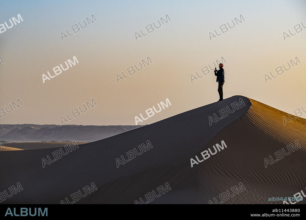 Man hiking through the sand dunes, Dirkou, Djado Plateau, Sahara, Niger, Africa.