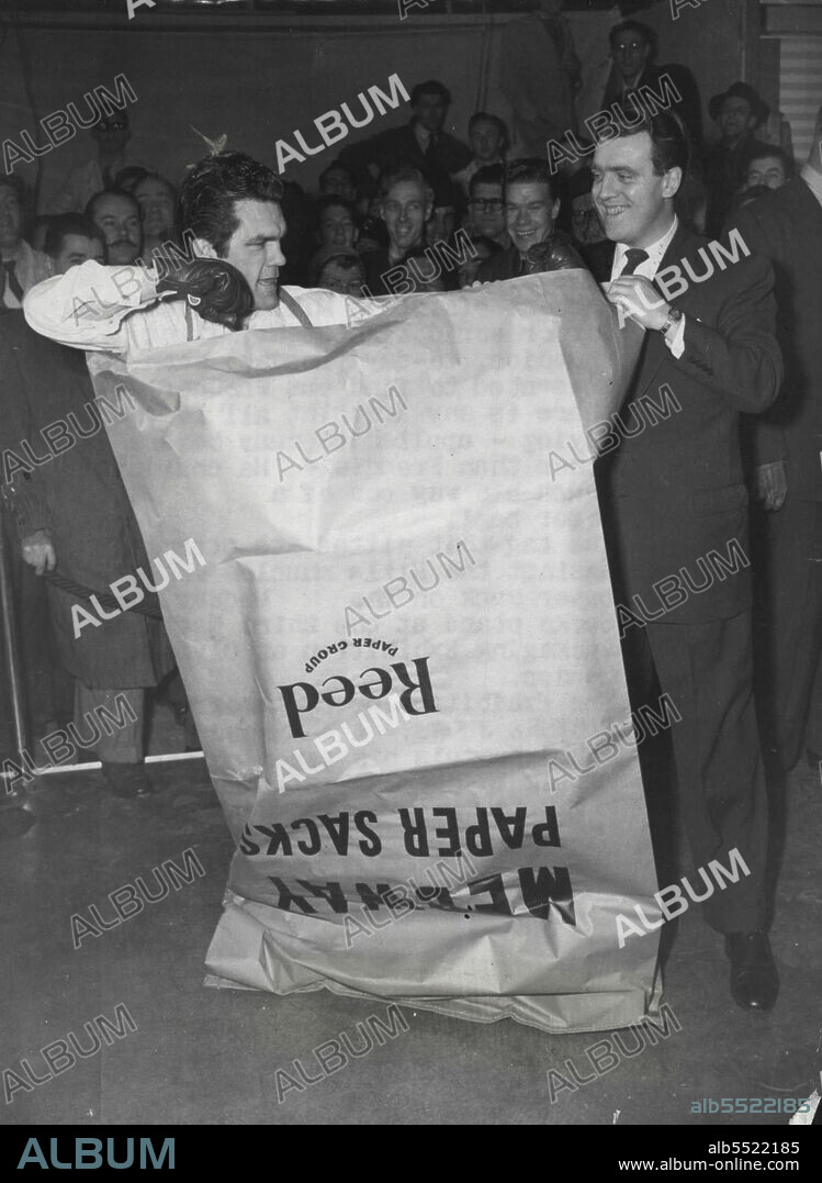 Freddie Mills Tries to Punch his way out of a Paper Bag -- A harassed Freddie Mills pummels his paper prison during to-day's test. On right is compere Eamonn Andrews, the radio commentator, who is himself an amateur heavyweight.The most difficult punch bag I have ever encountered was the comment of Freddie Mills, Britain's former world light heavyweight champion, to-day (Monday) when he consented to find out whether there is any truth at all in the saying - applied to many boxers other than Freddie - 'He couldn't punch his way out of a paper bag'. January 19, 1953.