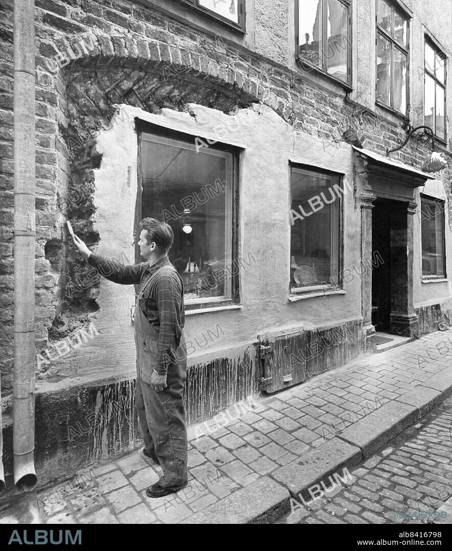 Stockholm 1960-08-26. Gamla stan. Här är Arne Eriksson sysselsatt med framknackningen av det medeltida bodfönstret. I Trångsund nr 8, hörnet av Ankargränd, i Gamla stan håller man just nu på att knacka bort gips for att få fram något riktigt medeltida fint, kanske ett butiksfönster ett sånt där med nedfälld lucka. Huset ägs av doktor Gustaf Nathanson och antikboden Snäckan bor i nedersta våningen.. Foto: Bengt Almquist / DN / TT / Kod: 1. ** SvD OUT **.