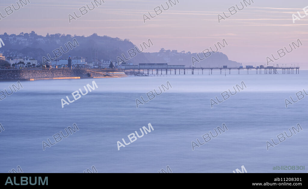 Sun making the sea wall glow on Teignmouth sea front with Teignmouth Pier behind, viewed from Shaldon, Devon, England, United Kingdom, Europe.