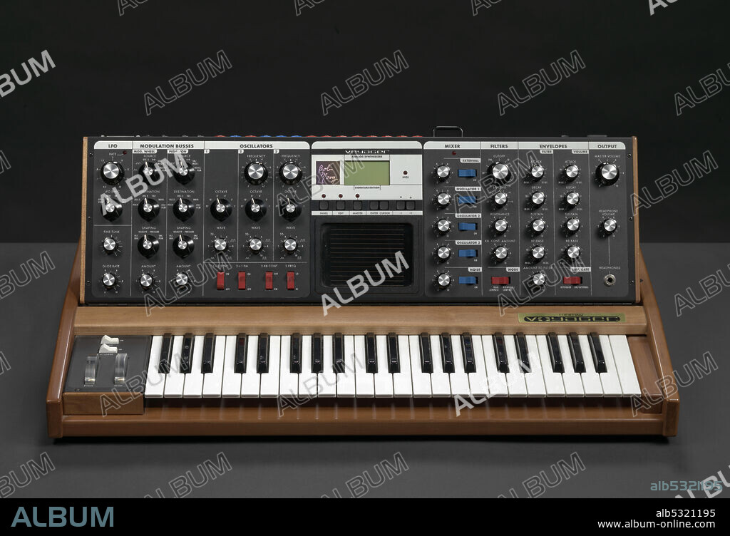 A Minimoog Voyager, a monophonic analog synthesizer, owned by record producer and artist J Dilla. The synthesizer features a small keyboard set into a wooden frame beneath a control panel. The control board consists of black knobs, red and blue switches, and two different sized screens. The control board has hinge and stand that allows it to be propped up to better face the user. A brass plaque appears above piano keys on right side, and reads, [minimoog®/voyager™]. On the back of the control panel is a label in the bottom left corner that reads, [MOOG MUSIC, Inc./ASHEVILLE, NC/minimoog® Voyager/SERIAL NO. 263].