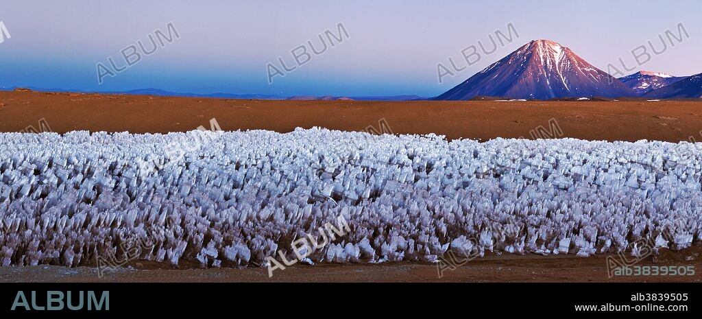 The spectacular Licancabur Volcano at the border between Chile and Bolivia. Licancabur appears in the morning twilight over an Andean ice field at an altitude of 5000 meters. The ice field in the foreground is a feature of high-altitude Andean plateaus known as ice penitentes. Licancabur reaches to 5920 meters. November 2011.