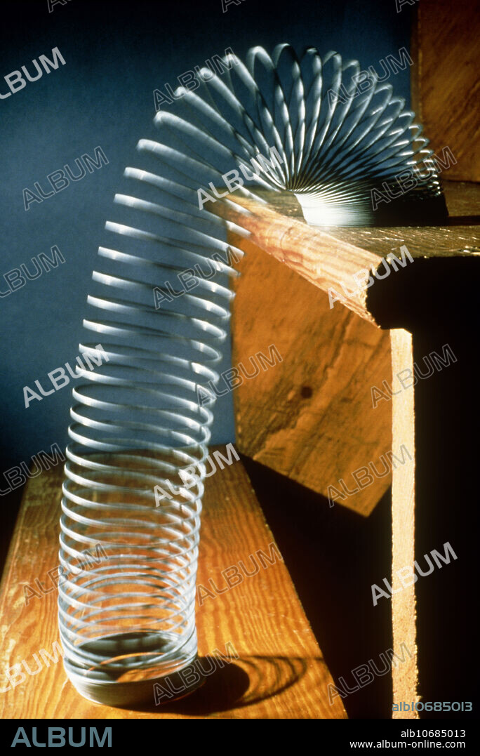 Slinky toy. View of a slinky toy moving down stairs. The slinky is a spring of metal which can move down stairs or ramps when pushed. As the top coil is pushed over the edge of the stair, the spring stretches, and pulls the rest of the slinky behind it. When the end of the slinky touches the lower stair, that end stops, and the rest of the slinky catches up. The momentum of this downward and forward movement means that the rear end overshoots the new base of the slinky, however, and starts a new cycle of movement by falling onto the next stair down. The potential energy in the spring is converted into kinetic energy during this motion.