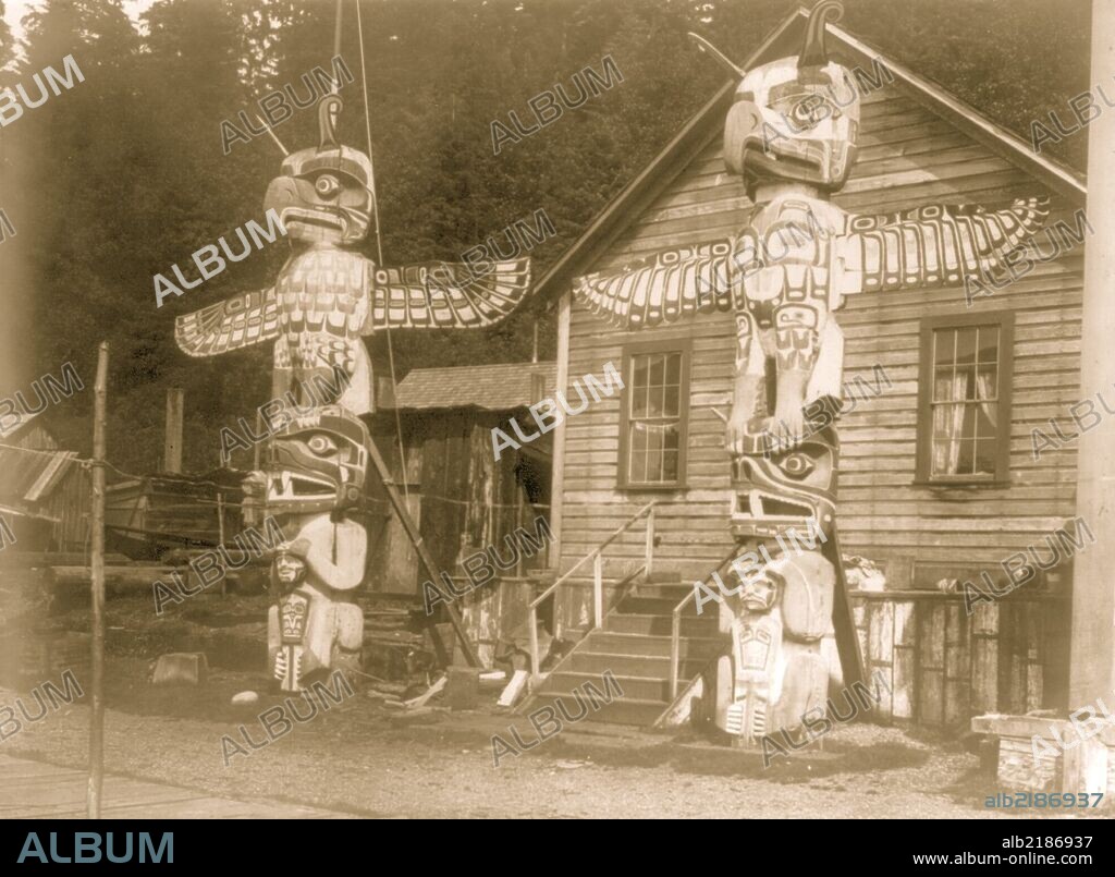 Two totem poles in front of a wood frame house in the Nimkish village Yilis, on Cormorant Island. Totem pole depicts an eagle representing the owner's paternal crest and a grizzly bear symbolizing the maternal one.