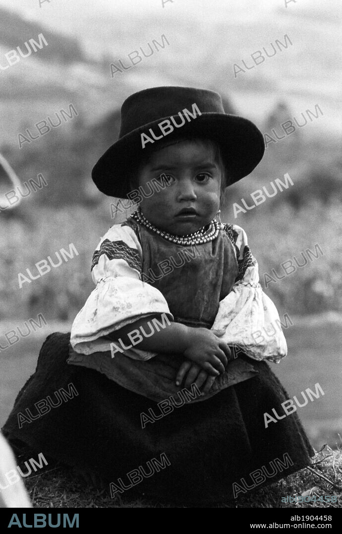 A Latin American girl wearing a traditional dress. A Latin American girl wearing a traditional dress, hat and necklace; she is posing outdoor. Latin America, 1970.