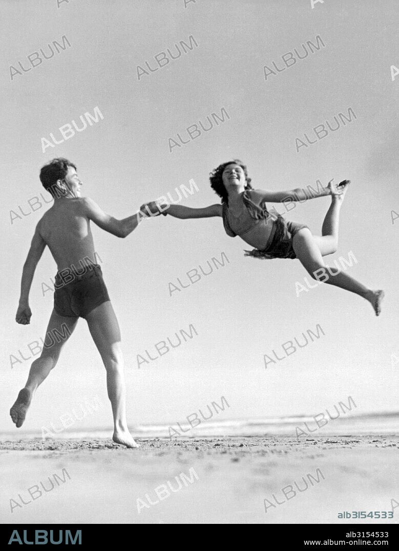 Long Beach, California:  c. 1933. A boy and a young girl do an acrobatic seaside exhibition on the beach.