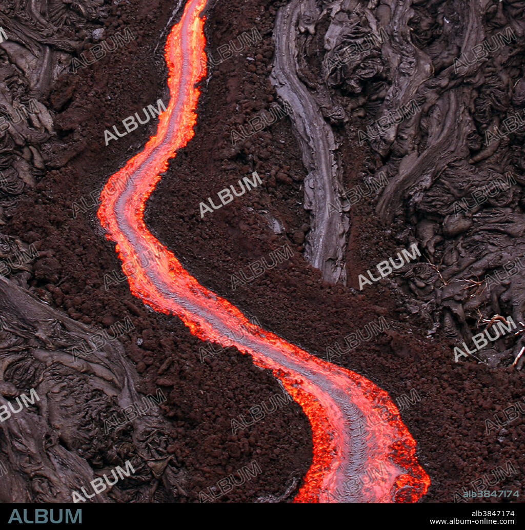 A strong channelized Aa lava flow (a lava river) on Kilauea volcano in Hawaii. Channels in Aa flows develop behind the tall advancing toes and help to push the sluggish lava forward. Note the smooth pahoehoe surrounding the channel. Also note the burned vegetation near the lava flow.