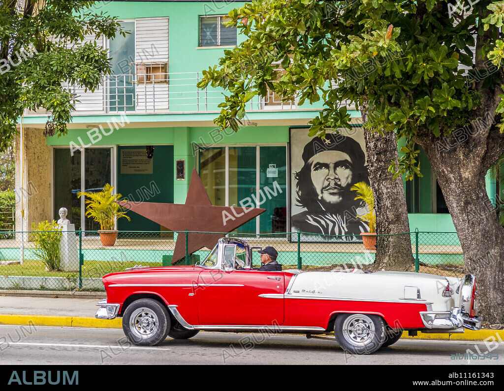 An old American car driving past a mural of Che Guevara, in Varadero, Cuba, West Indies, Central America.