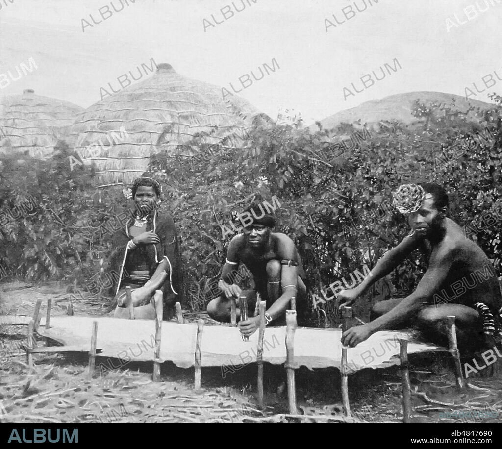 Magic Lantern slide circa 1880, Victorian/Edwardian, social history. The title of this image is 'Working like leather', a Zulu industry.  The workers of the empire, two Zulu men and a Zulu female making leather; Africa.