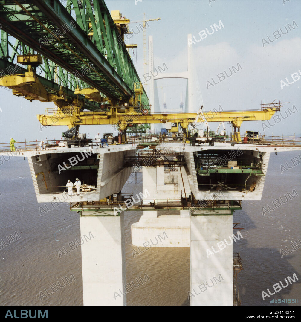 JOHN LAING PLC. A view of bridge deck units being installed during the construction of the Second Severn Crossing, showing a specially designed launch gantry overhead and two workers standing inside one of the deck units. The Second Severn Crossing took four years to build and was a joint civil engineering project between Laing Civil Engineering and the French company GTM. The work started in April 1992 and the opening ceremony later took place on 5th June 1996. The crossing is a cable-stayed bridge which stretches over 5000 metres across the River Severn connecting England and Wales, 3 miles downstream from the Severn Bridge which opened in 1966.
